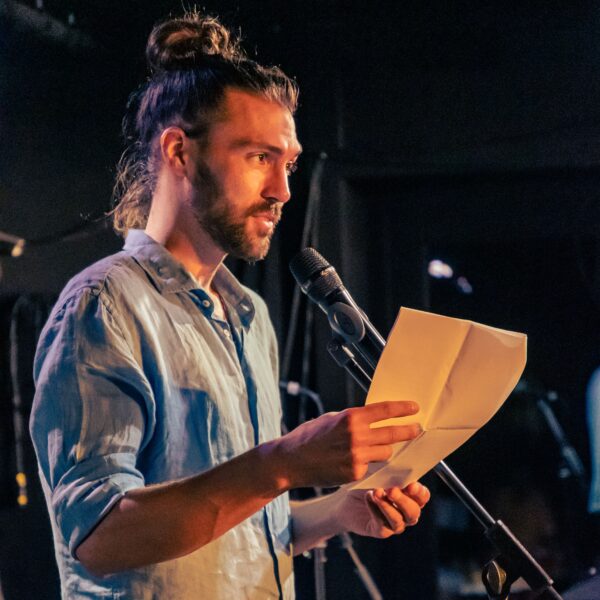 Dominik Heißler steht auf der Bühne und spricht ins Mikrofon.